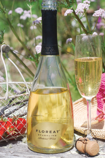 Bottle of open Floreat Wine stood on outside table next to full champagne flute glass of Floreat with plants and strawberries in background.